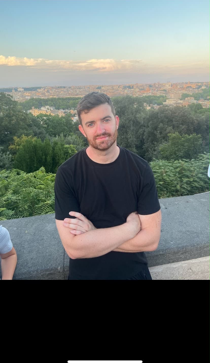 Conor, arms folded, on a terrace above a city at dusk